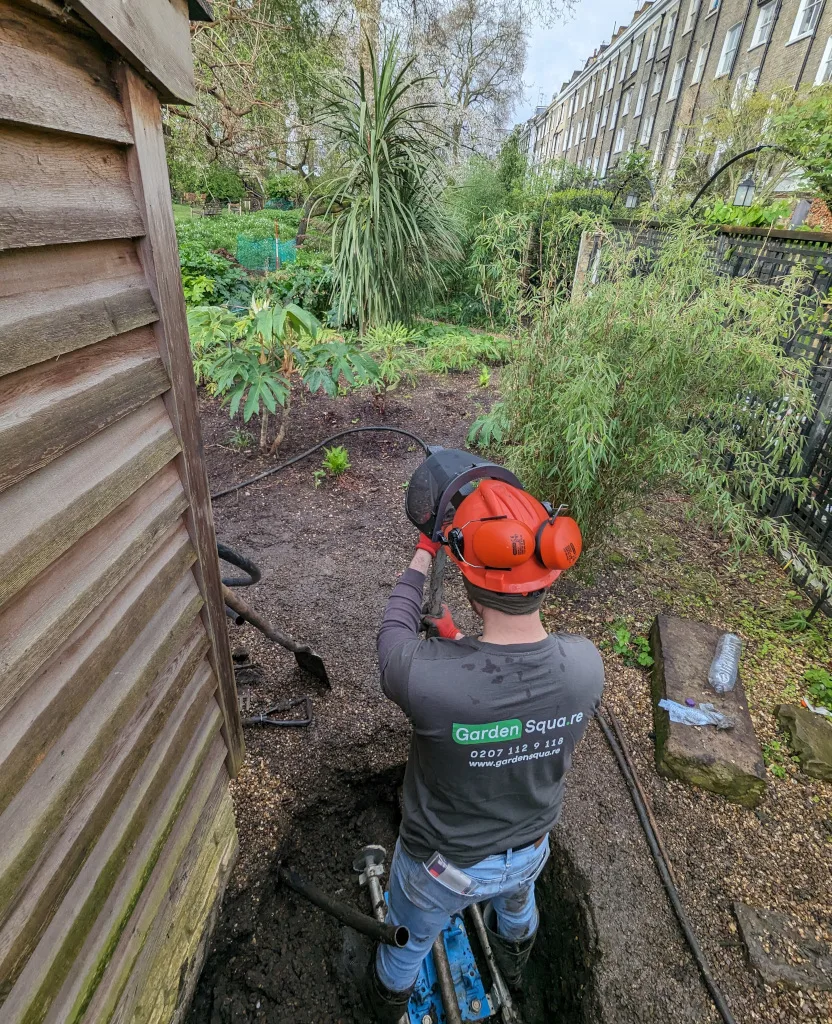 GardenSqua.re operative working in a narrow garden excavation beside a timber building